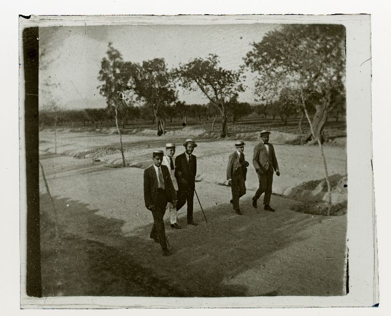 Grupo de cinco hombres con sombrero canotier paseando por un camino