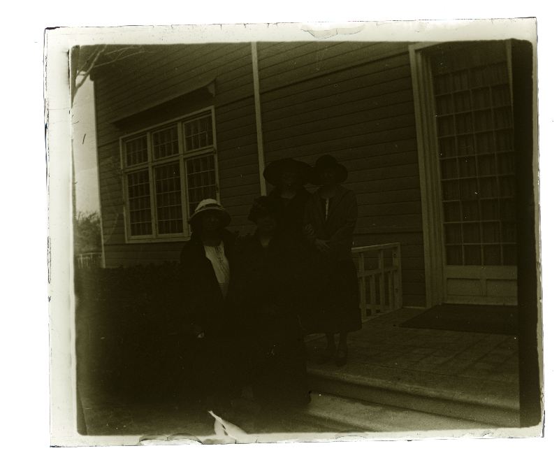 Retrato de cuatro señoras con sombrero a la entrada de una vivienda de madera