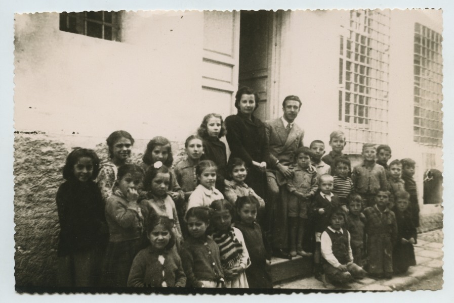 Retrato de grupo de niños y niñas con el maestro y la maestra en la puerta de la Escuela.