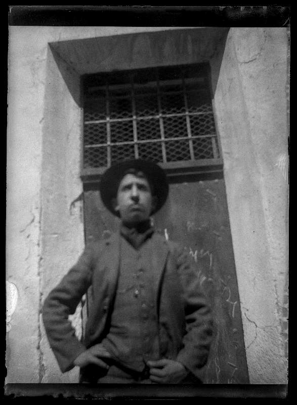 Retrato de medio cuerpo de un joven con sombrero frente a una puerta metálica