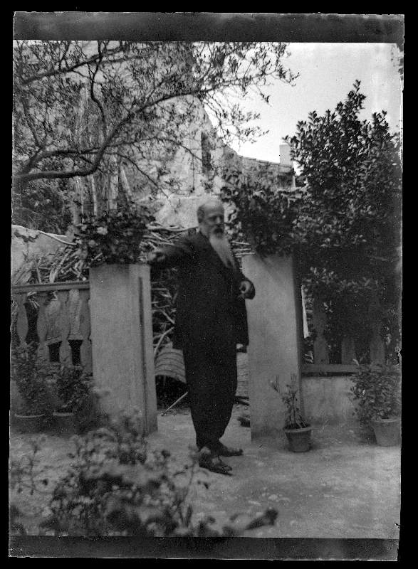 Retrato de cuerpo entero de un anciano con barba larga en el patio o jardín de una vivienda
