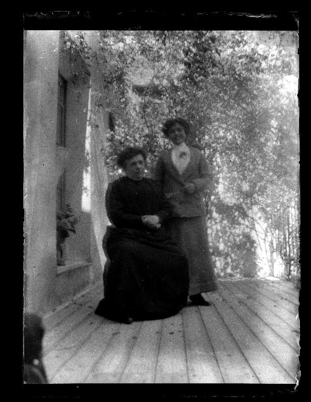 Retrato de dos mujeres en un porche con vegetación al fondo