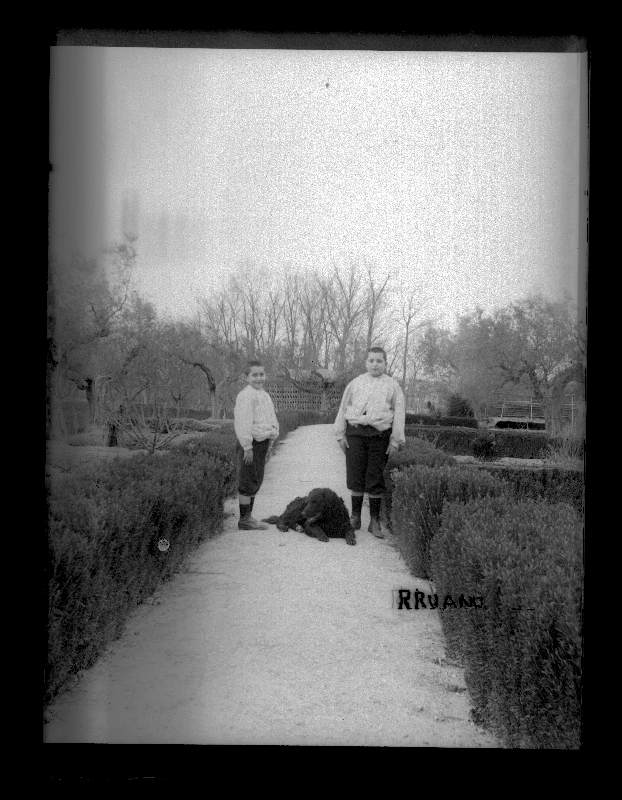 Retrato de los hermanos Manuel y Antonio Moxó Ruano con un perro negro en un jardín.