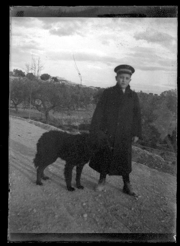 Retrato de Raimundo Moxó Ruano con abrigo oscuro y gorra de plato junto a un perro en un paseo por el campo