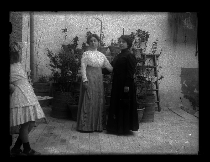 Retrato de cuerpo entero de dos mujeres en un patio mientras las observa una niña