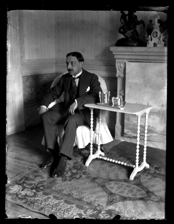 Retrato de un hombre, vestido de traje, sentado en el salón de una casa