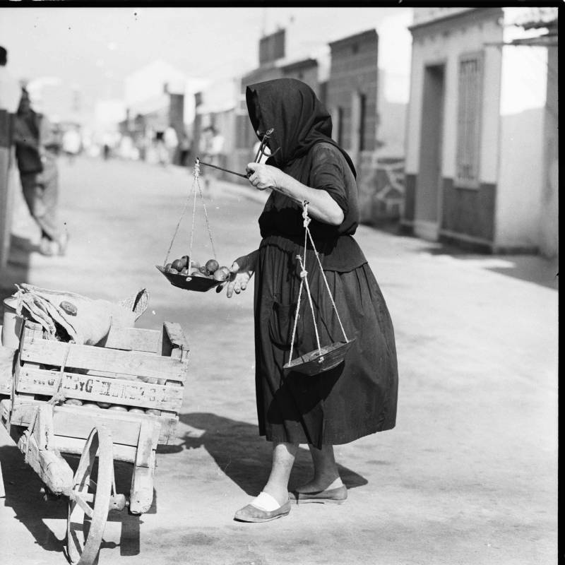 Una anciana vendedora ambulante pesando unos higos en una balanza.