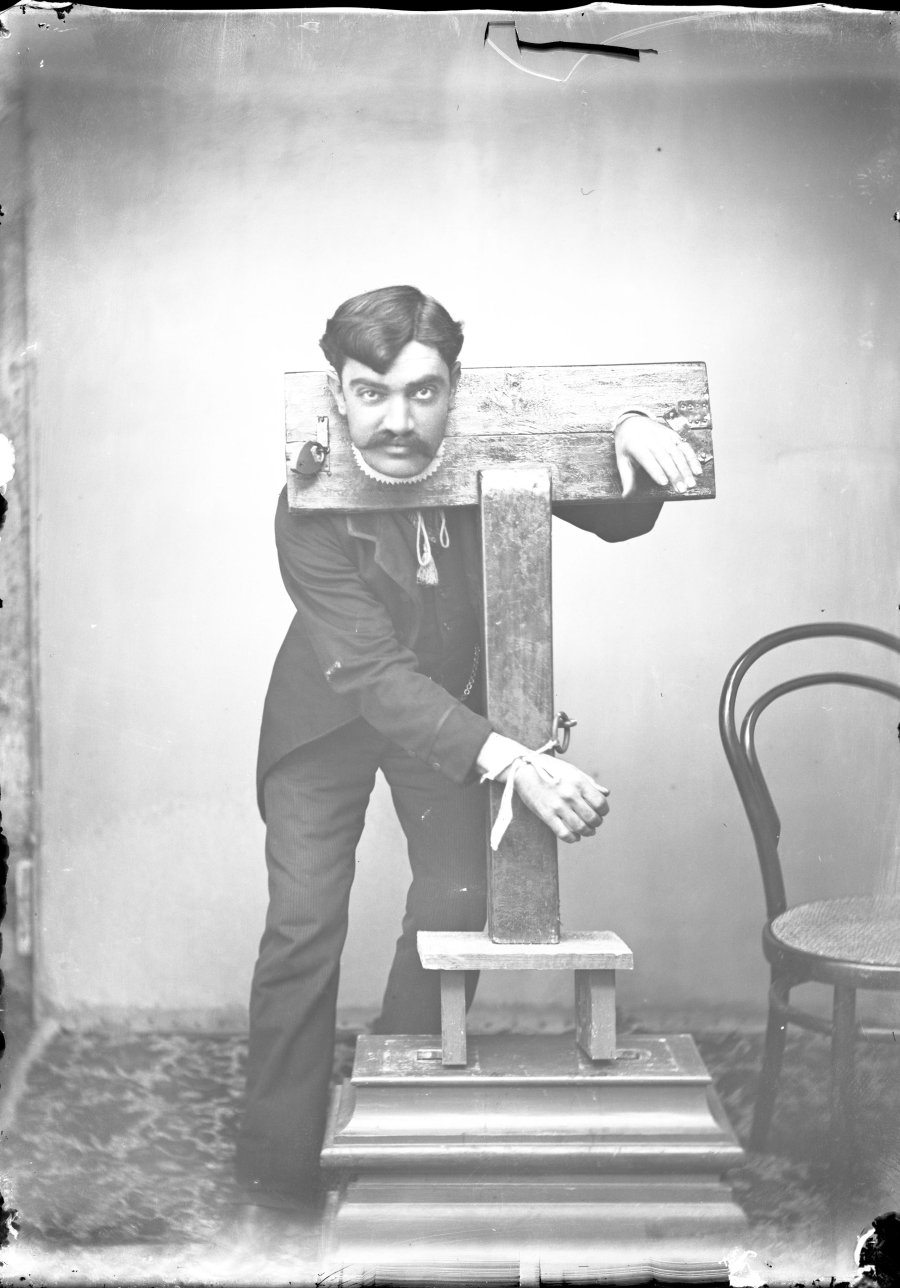 Retrato de estudio de un artista del escapismo con el cuello y ambas manos atrapadas en un cepo de madera