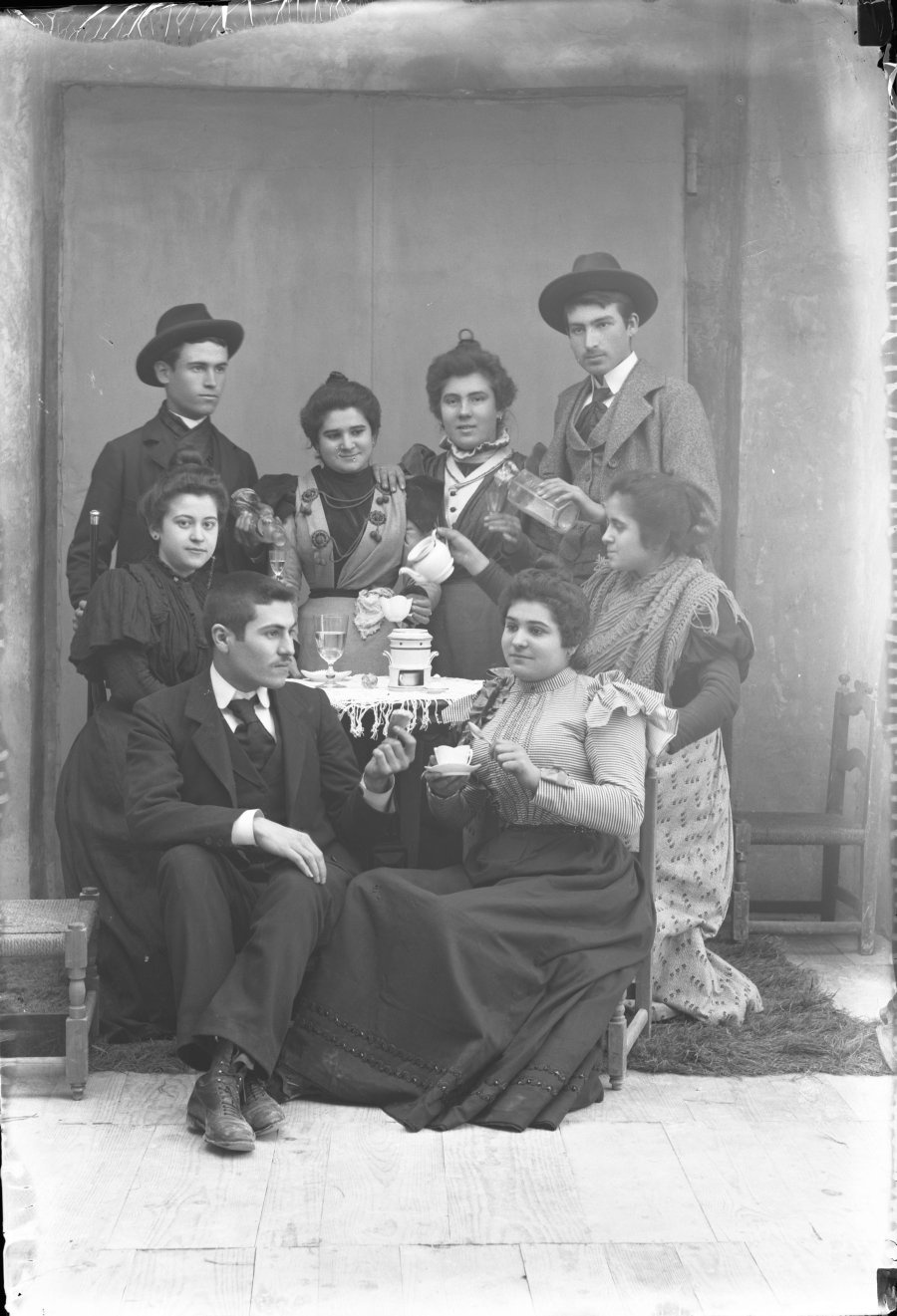 Retrato de estudio de un grupo de hombres y mujeres simulando una escena de reunión en torno a una mesa para tomar el té
