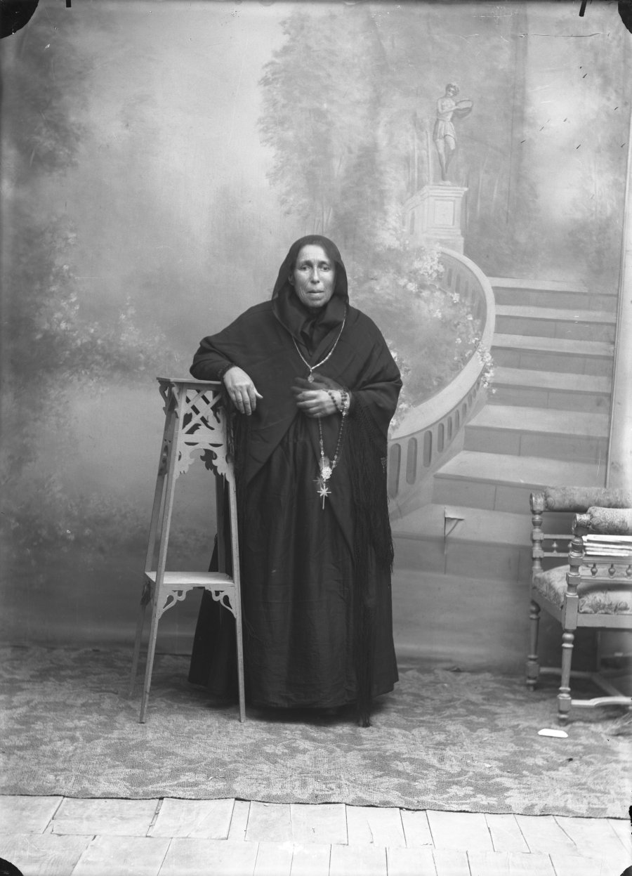 Retrato de estudio de una anciana de luto con rosario en la mano
