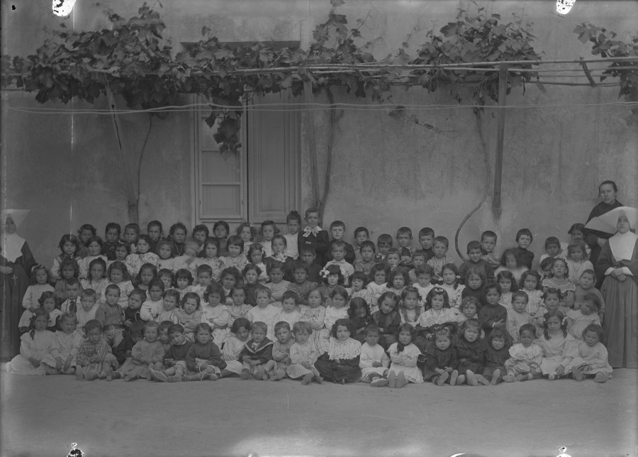 Retrato en exterior de un grupo de niñas y niños de distintas edades acompañadas por sus profesoras y algunas monjas