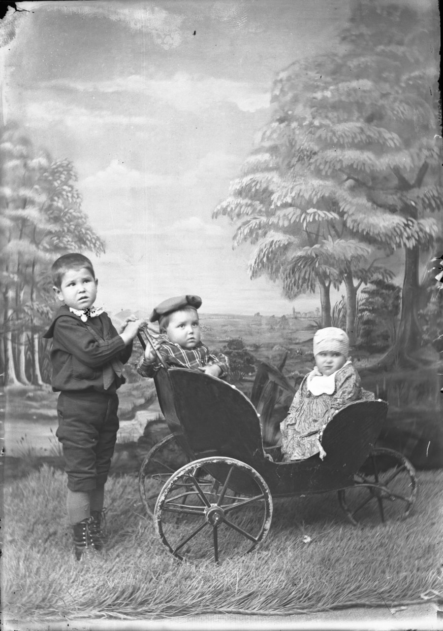 Retrato de estudio de tres niños representando un paseo por el campo con carricoche