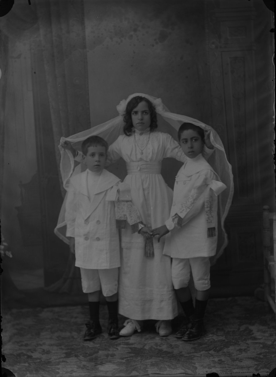 Retrato de estudio de una niña y dos niños vestidos de comunión
