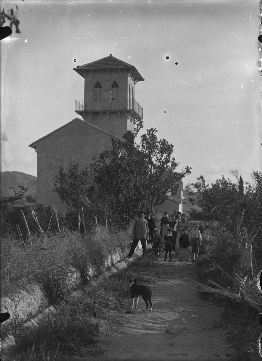 Retrato de un grupo de personas junto a una acequia en una parcela con casa torre en una zona de huerta de Totana