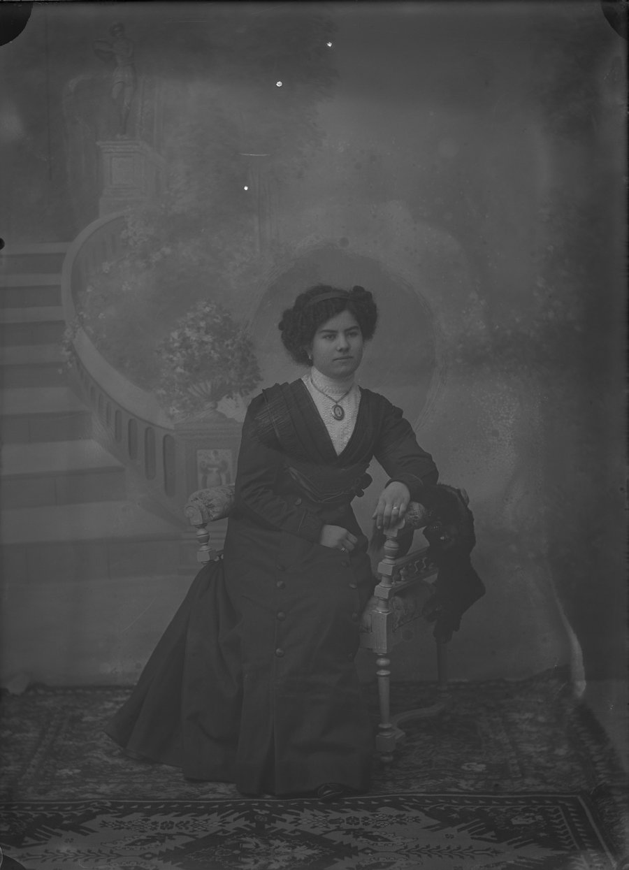 Retrato de estudio de una mujer joven con vestido negro y medallón de la Virgen