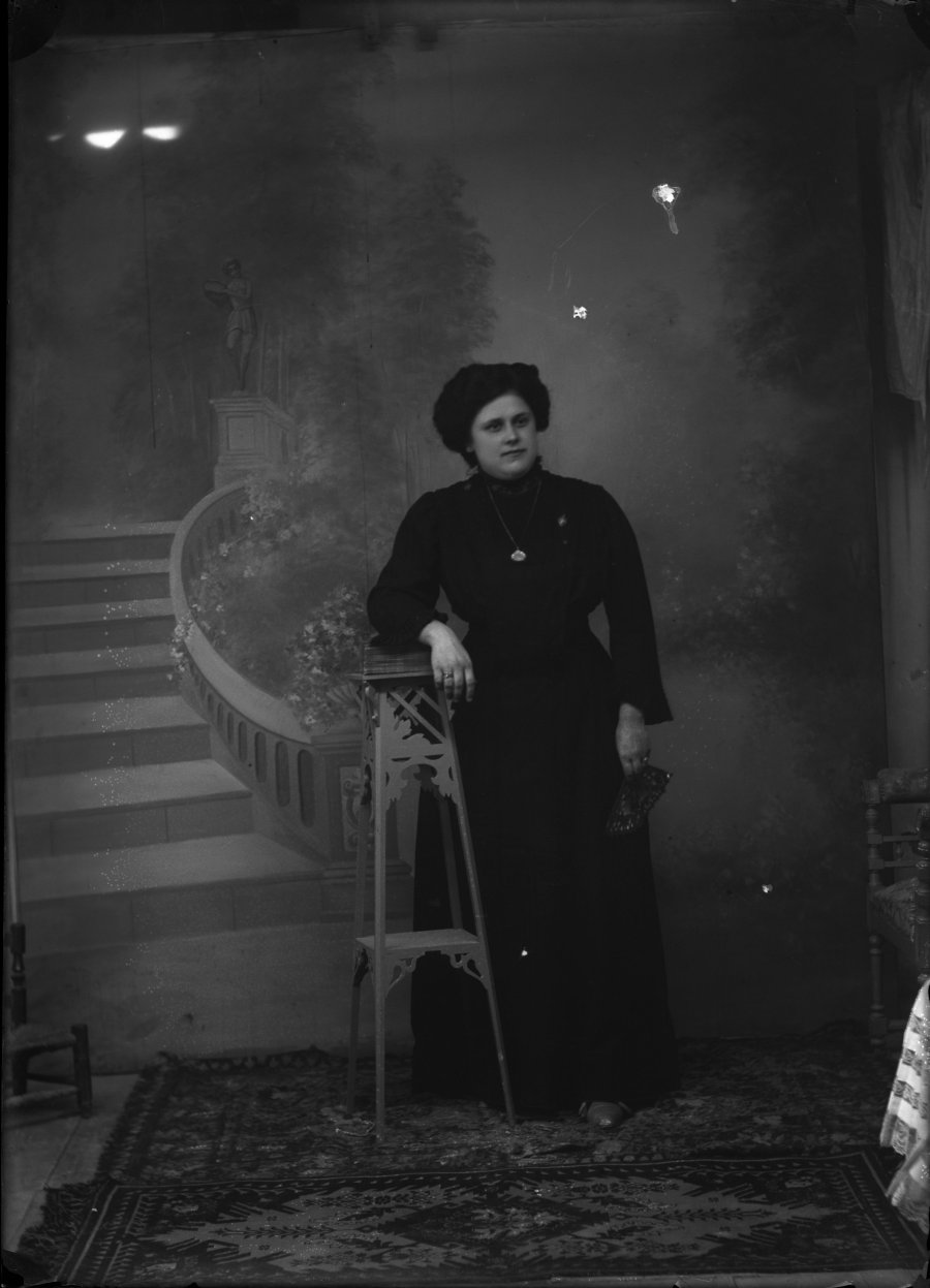 Retrato de estudio de una mujer de pie vestida de negro con medallón
