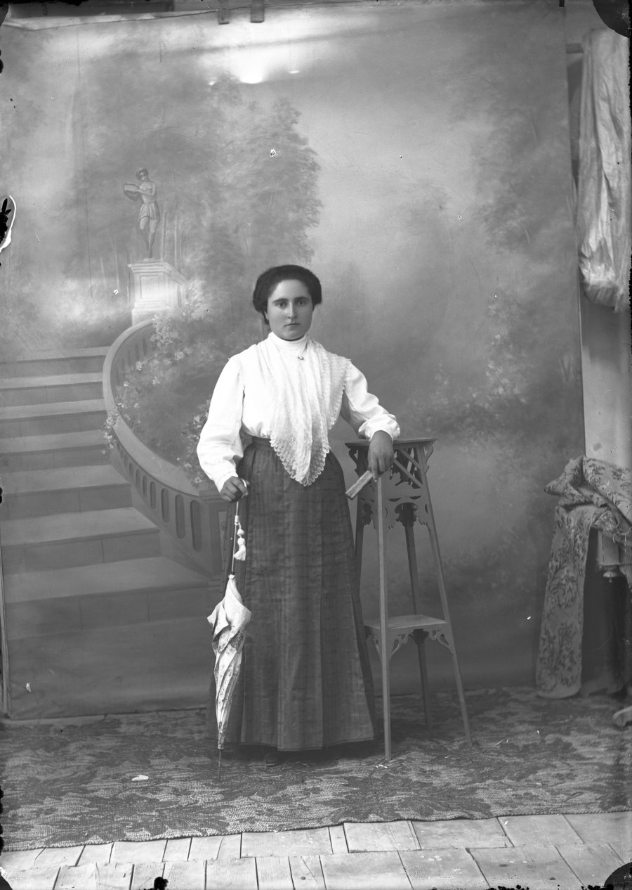 Retrato de estudio de una mujer joven con camisa blanca, falda oscura y sombrilla