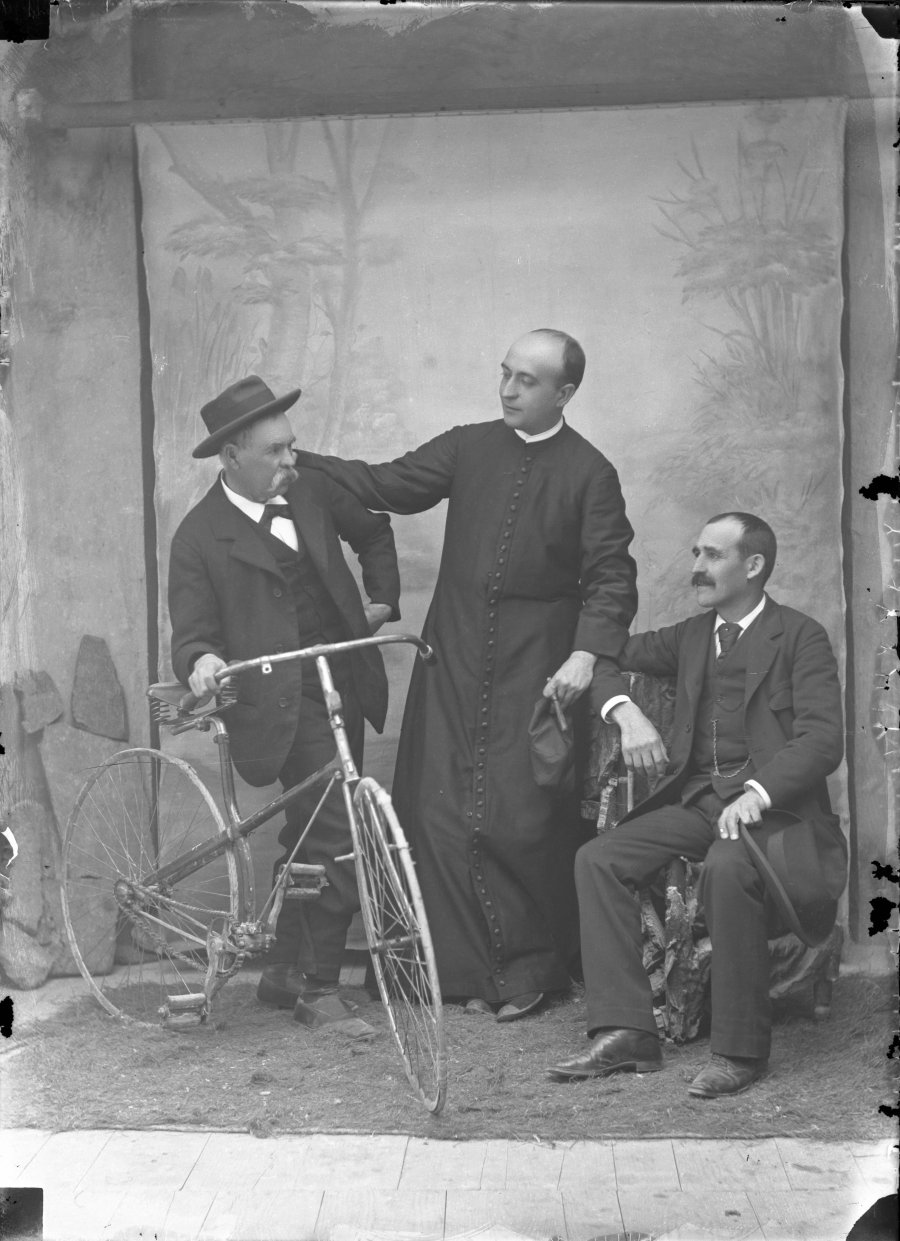 Retrato de estudio de tres hombres, uno de ellos sacerdote