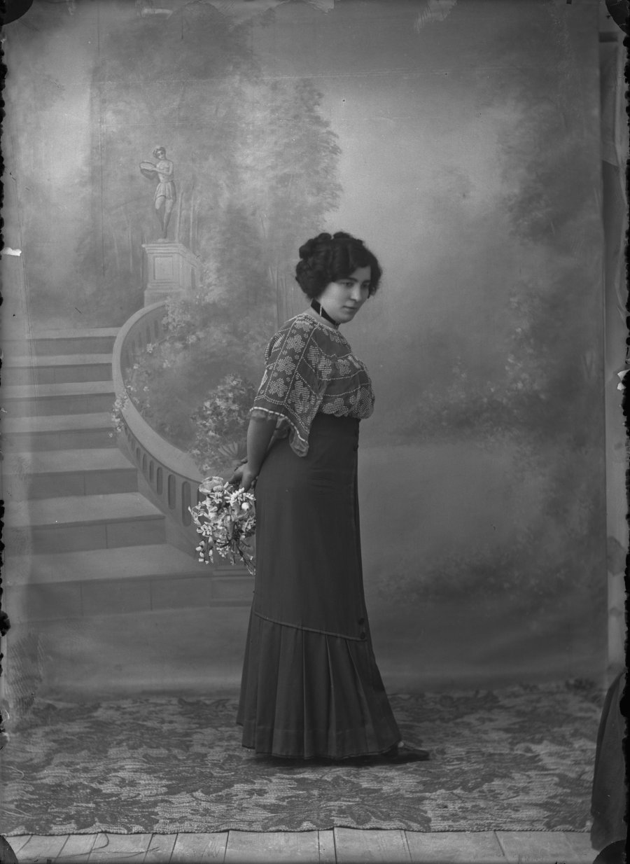 Retrato de estudio de una mujer joven de perfil con ramo y camisa de flores bordadas