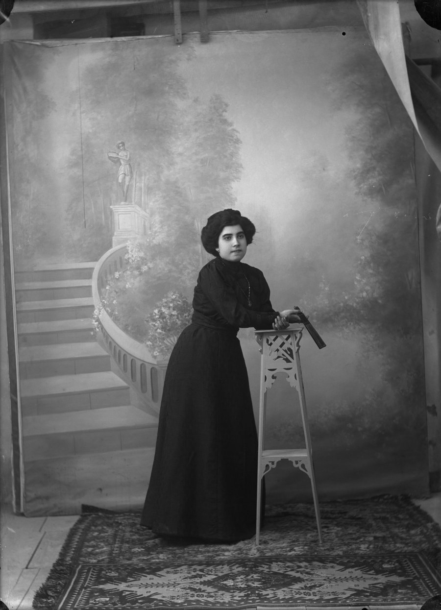 Retrato de estudio de una mujer joven con vestido negro apoyada en una rinconera