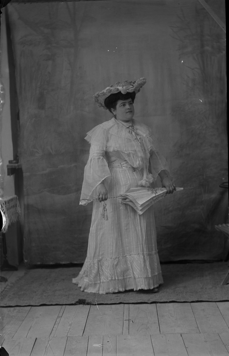 Retrato de estudio de una mujer joven con vestido blanco, sombrero y sombrilla
