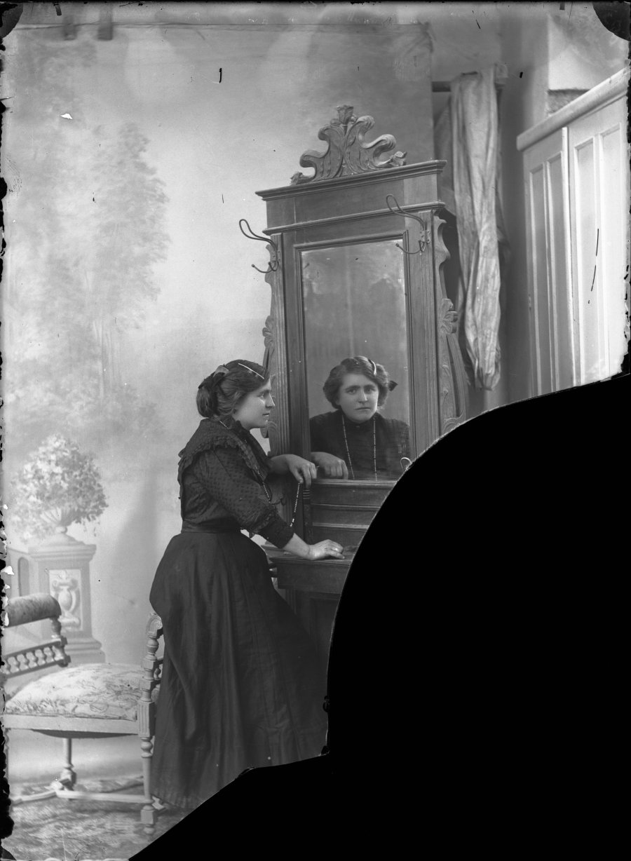 Retrato de estudio de una mujer joven con vestido oscuro junto a espejo vestidor