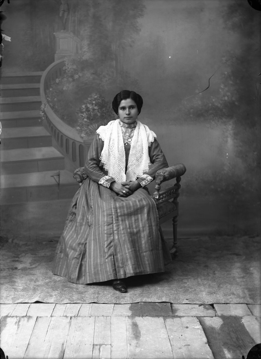 Retrato de estudio de una mujer joven sentada con vestido de rayas y chal de ganchillo