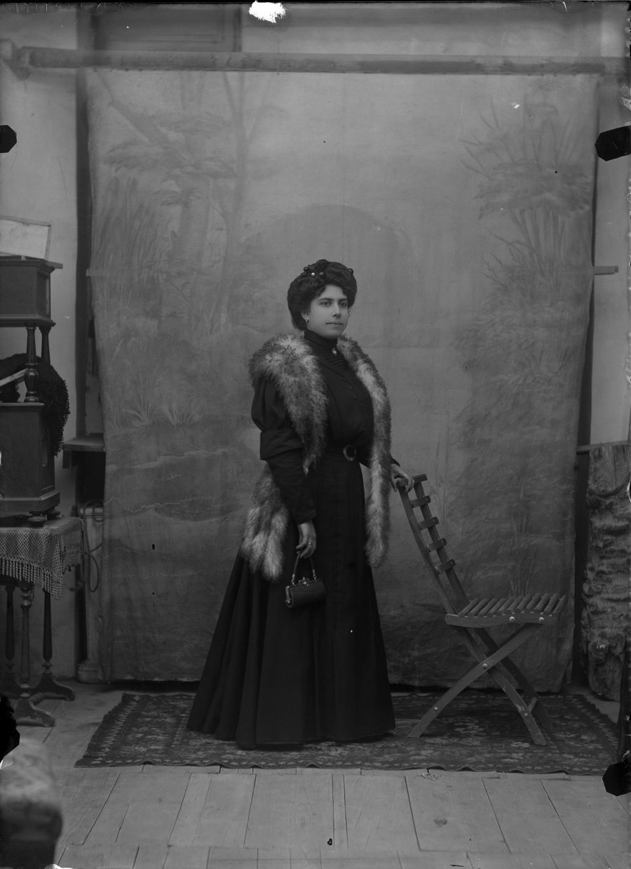 Retrato de estudio de una mujer joven con vestido negro, estola de piel y bolso de mano