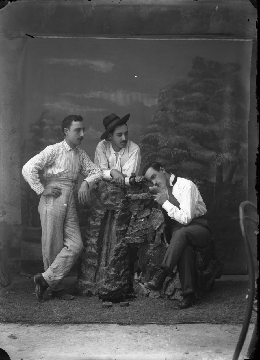 Retrato de estudio de tres hombres jóvenes en mangas de camisa con una botella de vino