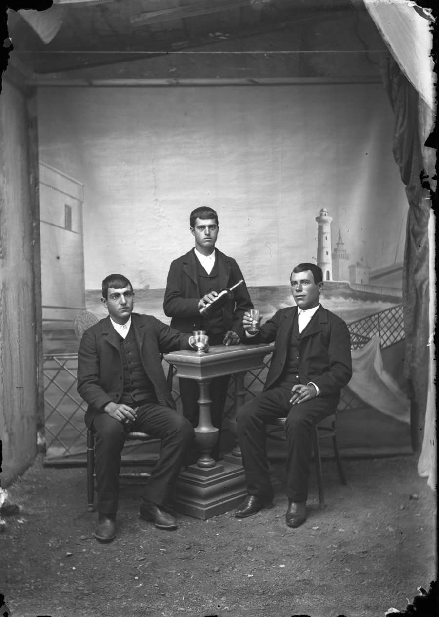 Retrato de estudio de tres hombres jóvenes bebiendo en torno a una mesa