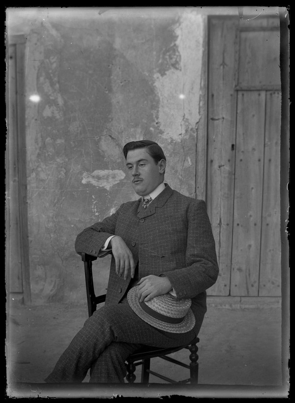 Retrato de un hombre sentado con traje de cuadros y sombrero de paja
