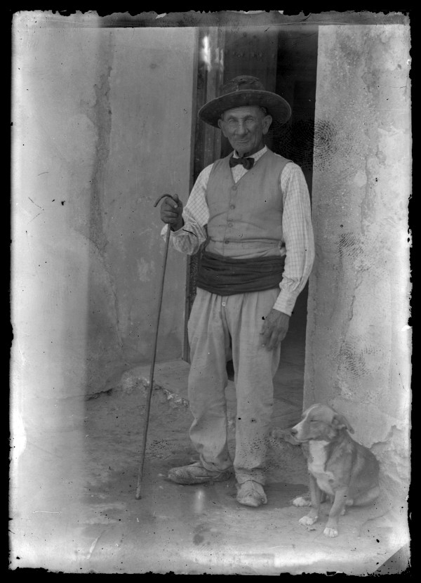 Retrato de cuerpo entero de un campesino anciano con perro junto a la puerta de una vivienda