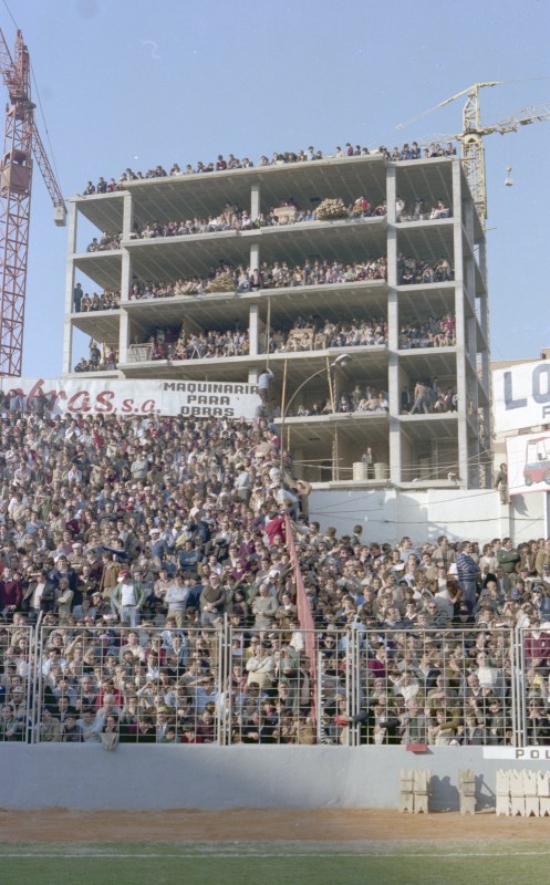 Grupos de aficionados contemplan, incluso desde un edificio en construcción, el partido de fútbol entre el Real Murcia y el Real Madrid en el campo de La Condomina.