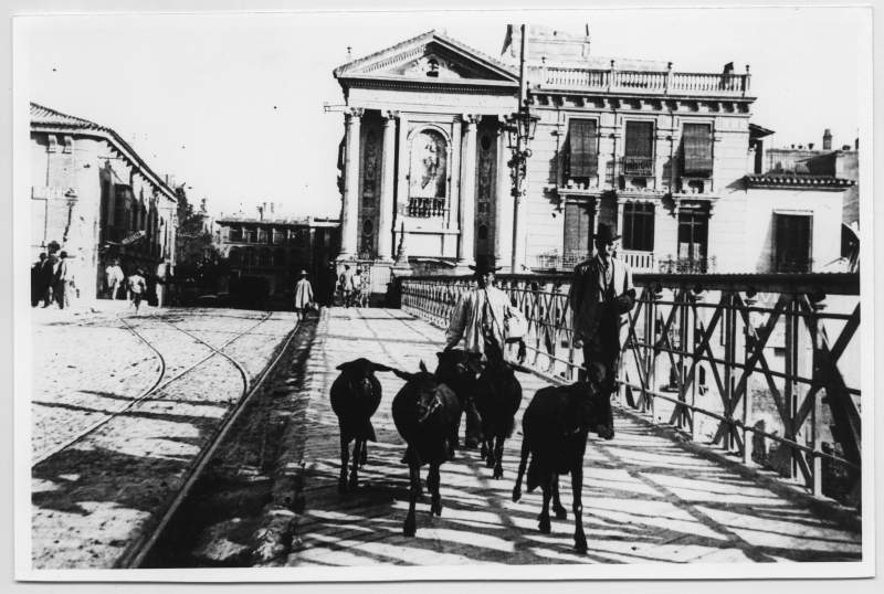 Reproducción de una fotografía de un lechero con sus cabras pasando por el Puente Viejo.