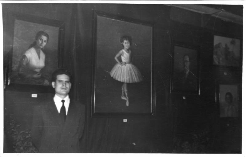 El artista Enrique G. Navarro ante sus cuadros en una exposición.