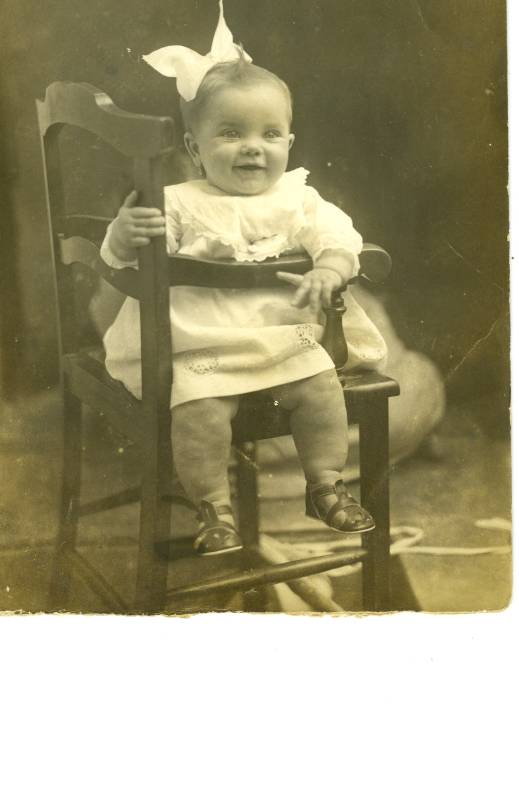 Retrato de bebé con lazo sentado en una trona.