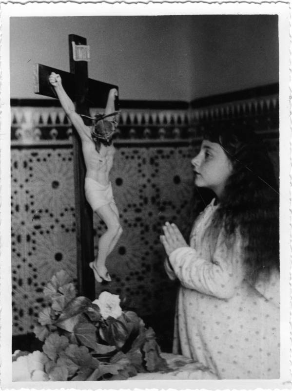 Retrato de niña rezando ante un crucifijo.