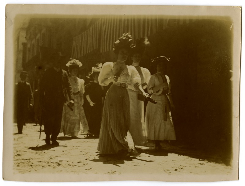 Tres mujeres jóvenes, con traje de paseo y sombrero, por una calle de Murcia