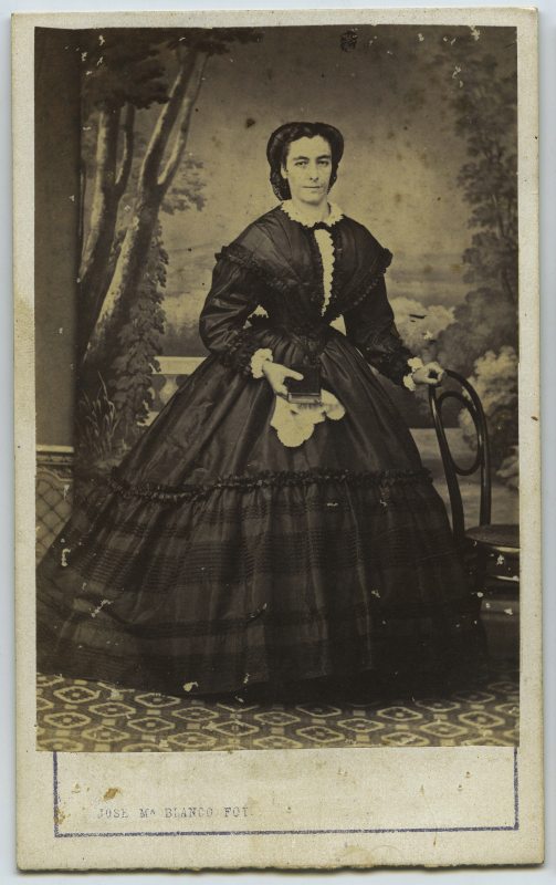 Retrato de estudio de una mujer de pie con vestido largo negro con miriñaque