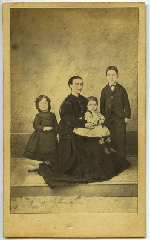 Retrato de estudio de una mujer sentada y tres niños vestidos de negro