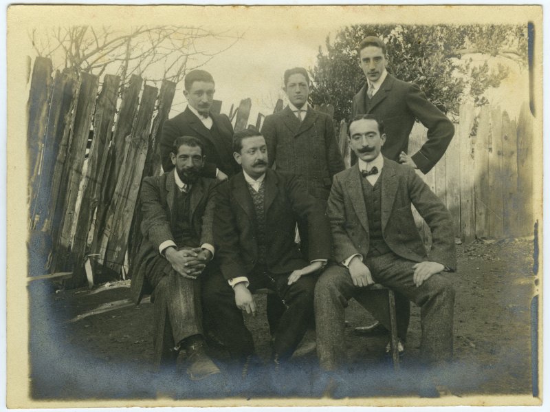Retrato de seis hombres posando en el patio de una casa de campo