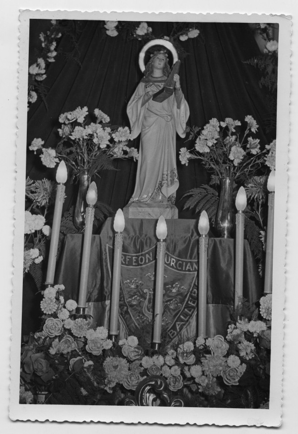Reportaje fotográfico de un altar con estatua, probablemente Santa Cecilia, y escudo del Orfeón Murciano Fernández Caballero.