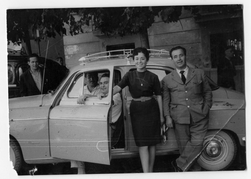 Retrato de Antonio González sentado al volante de un coche con varias personas alrededor