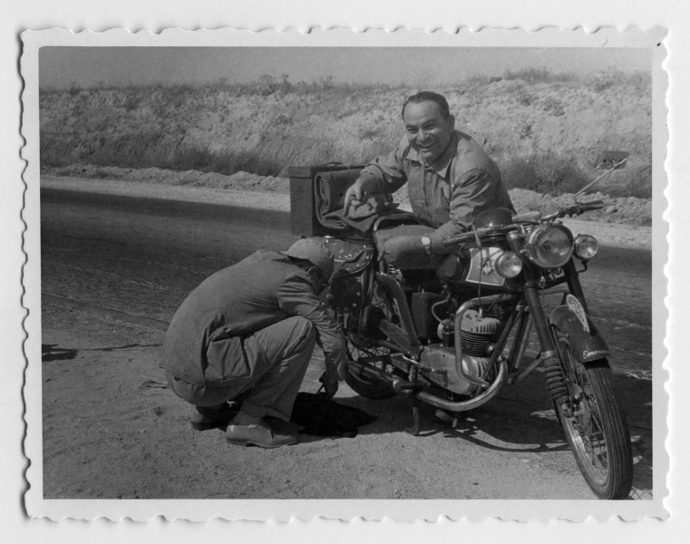 Retrato de Francisco Suárez junto a su motocicleta mientras es reparada por otro hombre