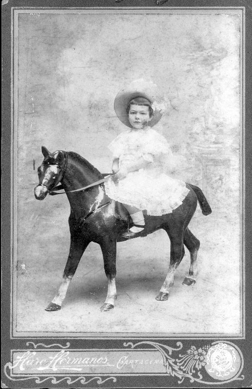 Retrato de niña sobre caballo de madera.