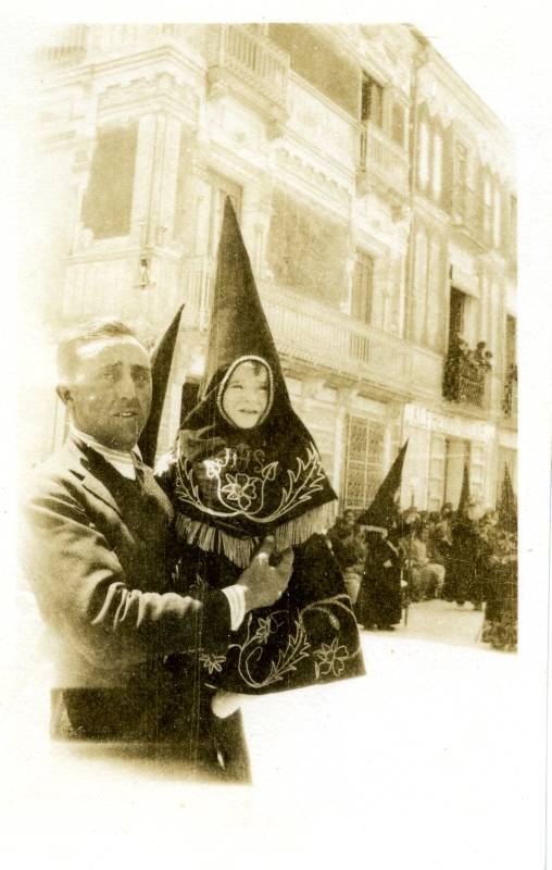 Un hombre desconocido con un niño en brazos vestido con la túnica de nazareno de la Real Cofradía de Jesús Nazareno de Jumilla.