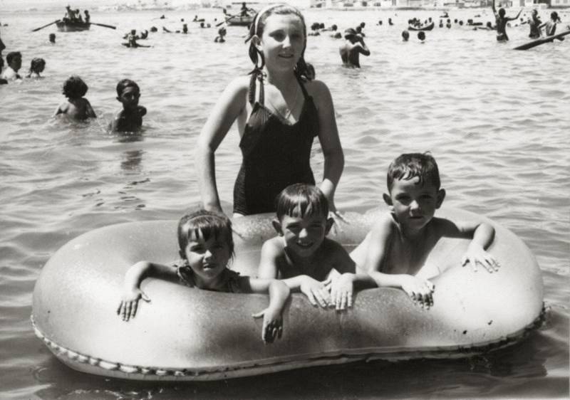  Joven lumbrerense acompañada por tres niños en escena de playa, posiblemente en Águilas