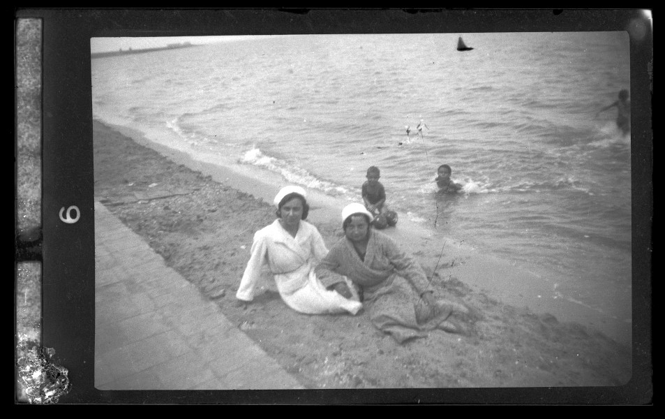 Retrato de dos mujeres con gorro y albornoz sentadas en la orilla de la playa